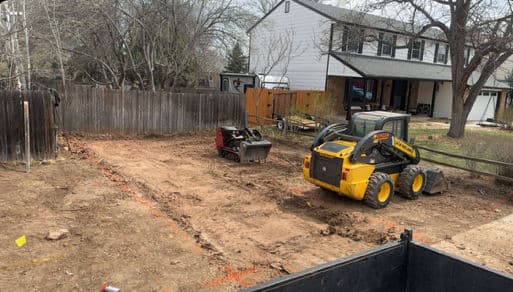 Construction site with heavy machinery preparing a backyard for landscaping.