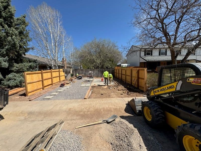 Construction workers on a gravel pathway installing wooden fences in a residential area.