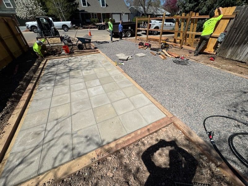 Construction site with workers laying paver stones and gravel for a new patio or walkway.