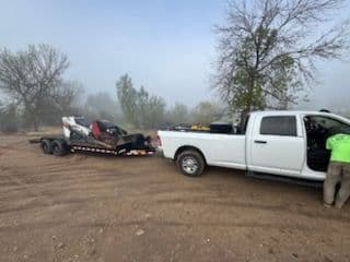 White truck towing a trailer with equipment in a foggy rural setting.