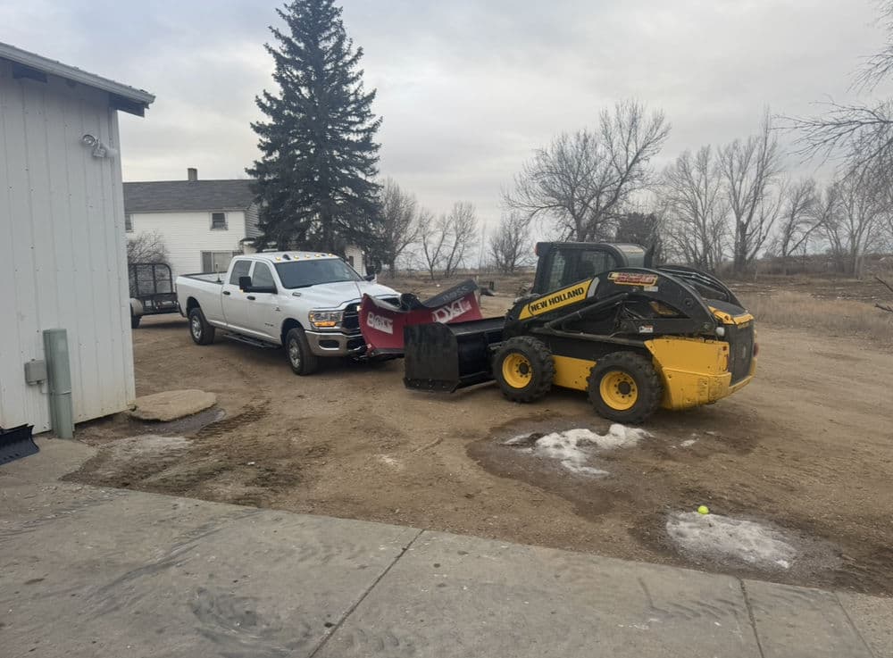 Pickup truck and skid steer loader with snowplow attachment on a rural property.