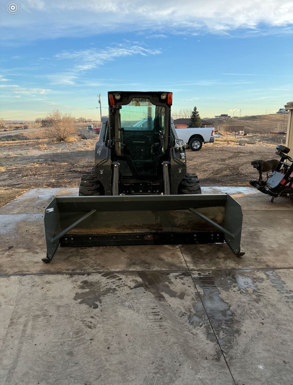 Skid steer loader with a snowplow attachment on a driveway in a rural setting.